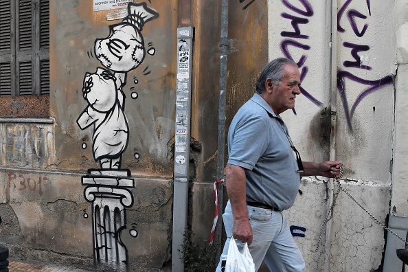A man walks past a graffito depicting a bag of money with a euro currency symbol on a crumbling greek statue and column in Athens on September 12, 2018. (Getty Images) 