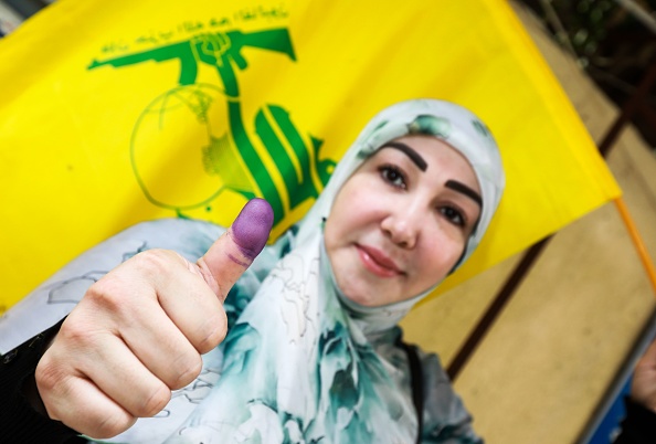 A Lebanese Shiite woman flashes her ink-stained thumb and waves a flag of the Shiite Hezbollah movement after voting at a polling station in the capital Beirut on May 6, 2018, as the country votes in the first parliamentary election in nine years. (Getty)
