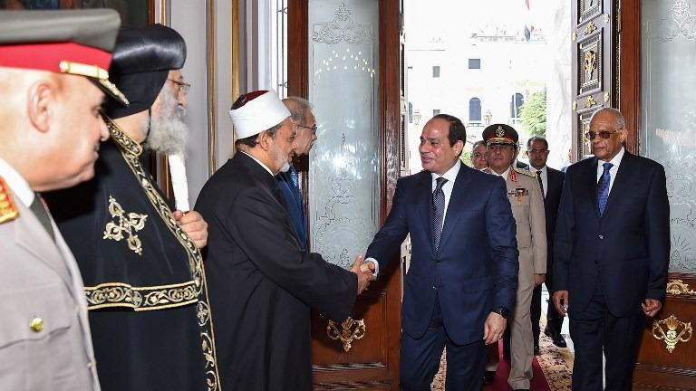 "3-	A handout picture released by the Egyptian Presidency on June 2, 2018 shows Egyptian President Abdel Fatah al-Sisi (Center) shaking hands with Grand Imam of Al-Azhar Sheikh Ahmed al-Tayeb (3rd-Left), as him and Prime Minister Sherif Ismail (4th-Left), Coptic Orthodox Pope of Alexandria Tawadros II (2nd-Left), and Defence Minister Sedky Sobhy (Left) receive him and Parliament Speaker Ali Abdel Aal (Right) ahead of Sisi's swearing-in ceremony for a second four-year term in office, at parliament headquarters in the capital Cairo. (EGYPTIAN PRESIDENCY / AFP)"